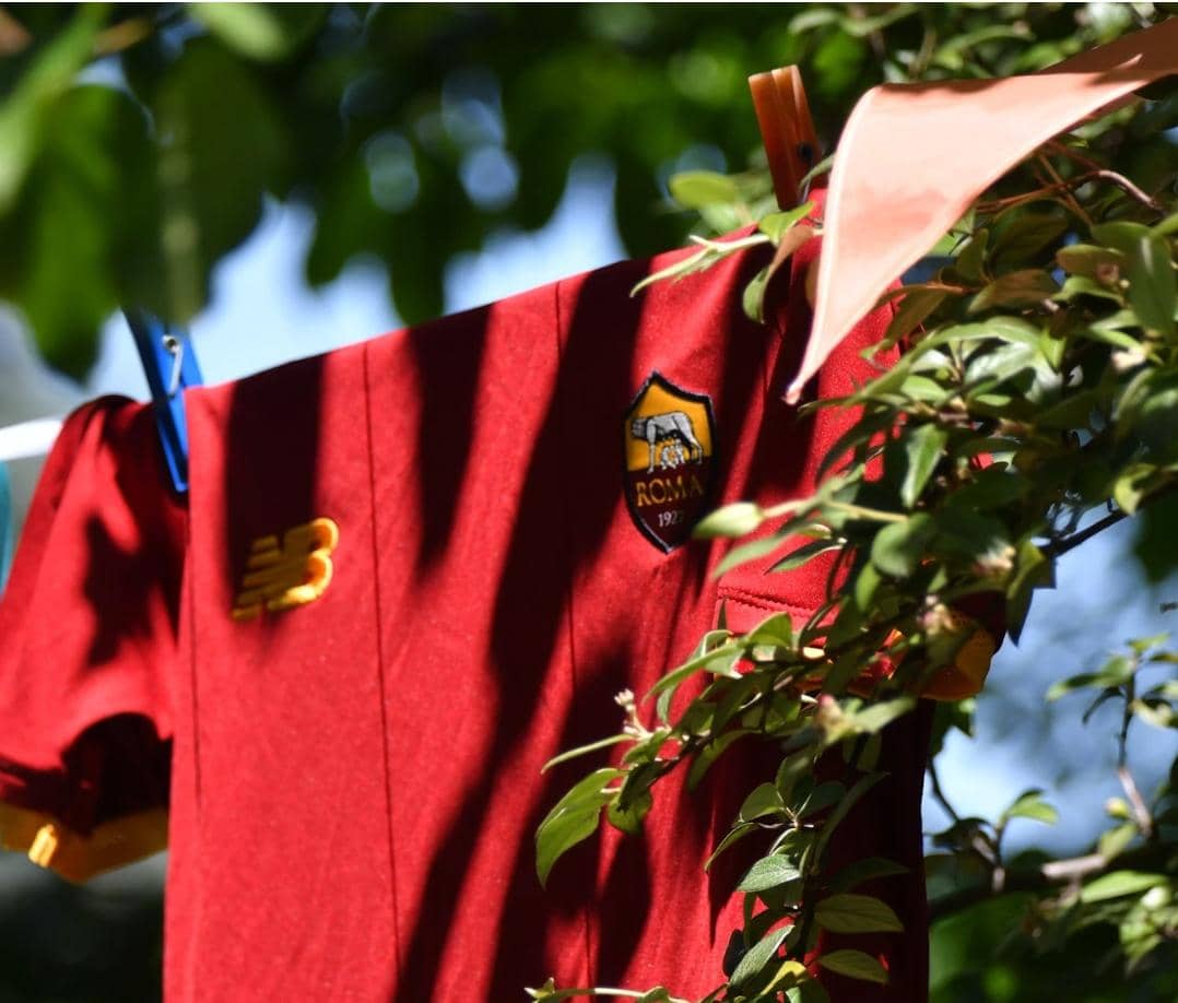 Jersey berwarna merah marun dengan logo klub sepak bola tergantung di tali jemuran di antara dedaunan hijau.
