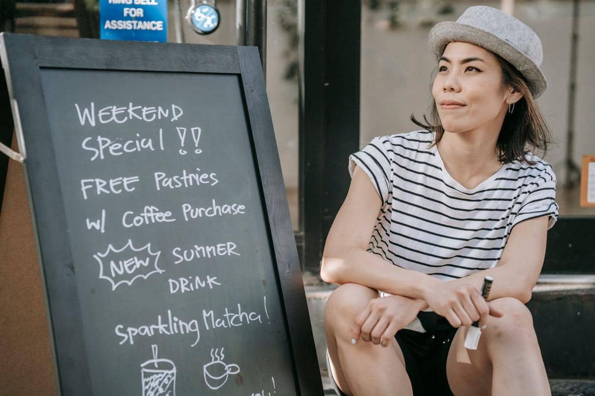 ilustrasi seorang wanita duduk di samping papan menu kedai kopi yang mempromosikan menu spesial
