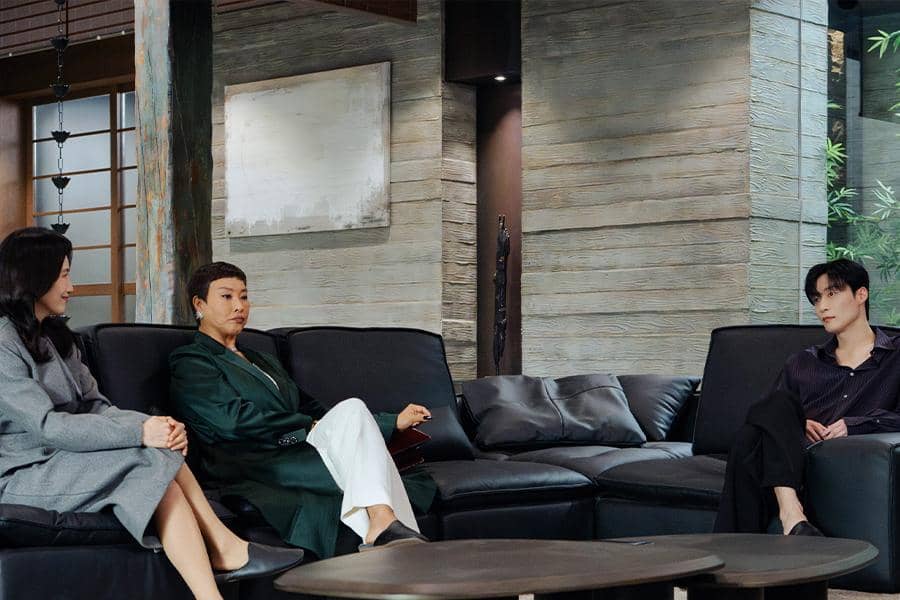 Tiga karakter dalam drama Korea My Royal Nemesis duduk di ruang tamu modern dengan suasana tegang dan pencahayaan hangat.