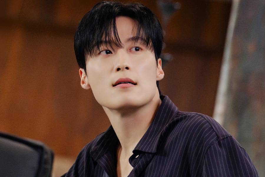 Seorang aktor Korea mengenakan kemeja bergaris gelap menatap ke arah atas dalam cuplikan drama My Royal Nemesis.