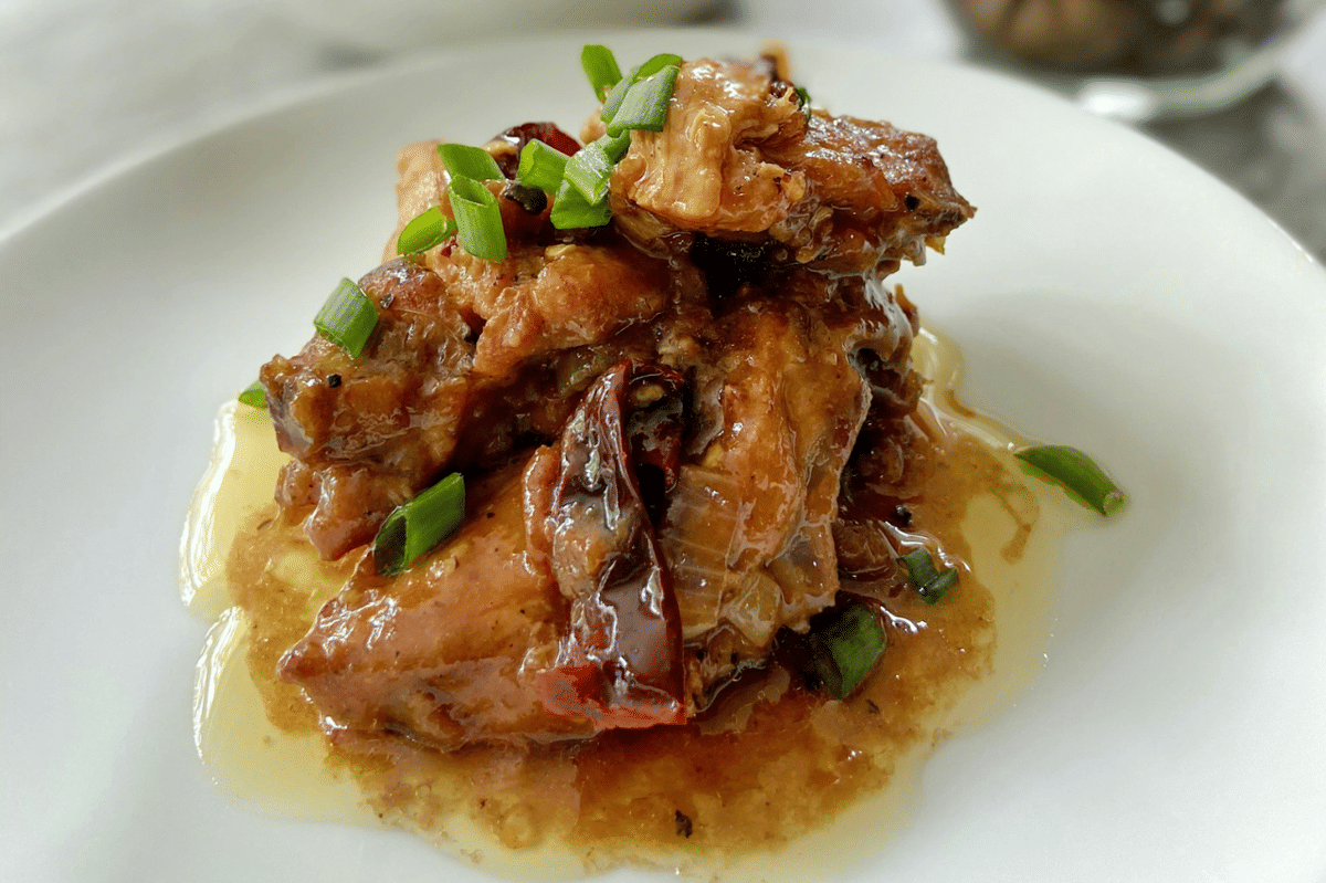 Terong isi ayam disajikan di atas piring putih dengan saus kental berwarna cokelat dan taburan daun bawang segar di atasnya.