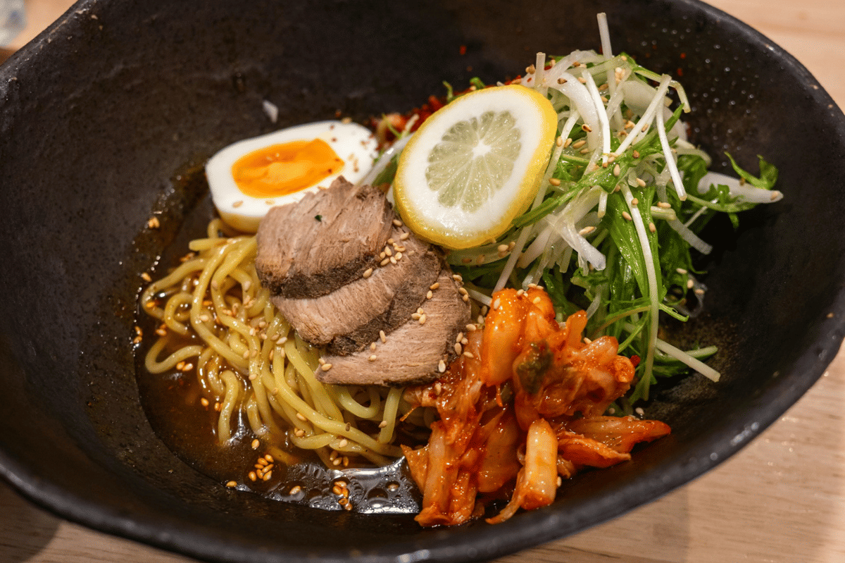 Semangkuk buldak steak ramen dengan potongan daging sapi, telur setengah matang, irisan lemon, sayuran segar, dan kimchi pedas.