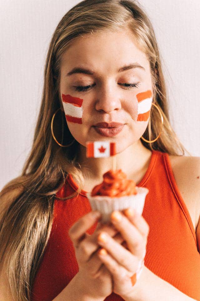 Seorang pendukung sepak bola mengenakan kaus merah dengan cat wajah bergambar bendera di pipi sambil memegang cupcake kecil.