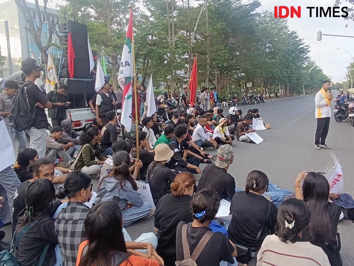Mahasiswa Aliansi Perisai duduk di jalan saat melakukan aksi demonstrasi di depan Kantor DPRD NTT, Kota Kupang, dengan membawa spanduk dan bendera.