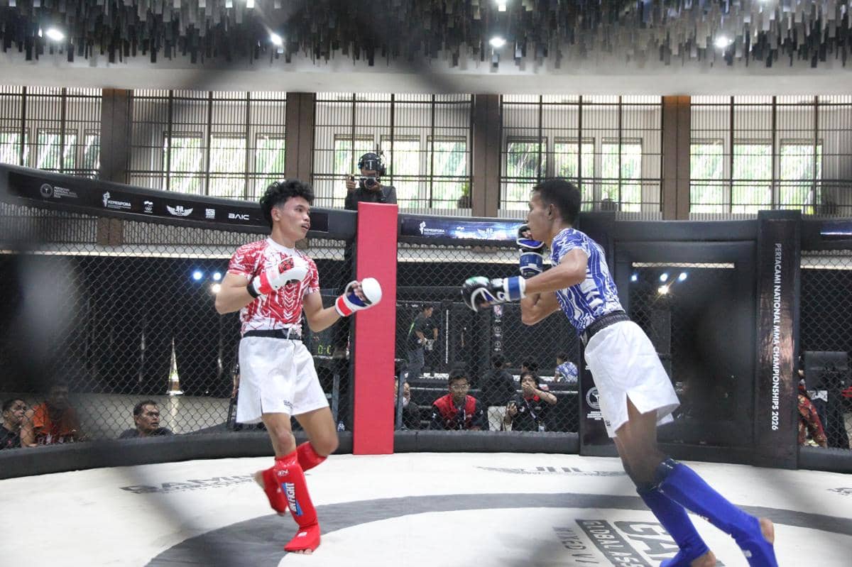 Dua atlet MMA bertanding di dalam arena oktagon pada Kejurnas MMA 2026 di Bogor, mengenakan pelindung berwarna merah dan biru.