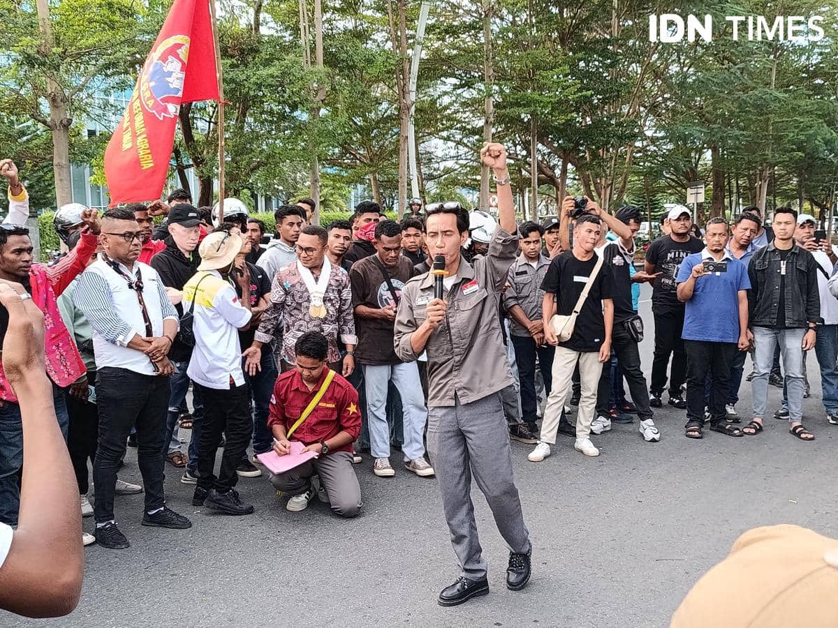 Seorang orator memimpin aksi demo mahasiswa Aliansi Perisai di depan Kantor DPRD NTT, Kota Kupang, dengan massa membawa bendera merah.