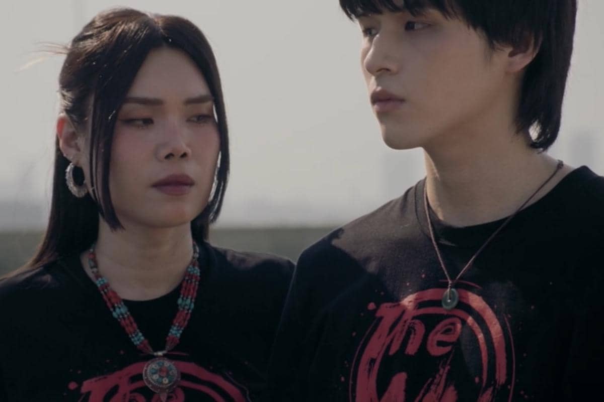 Dua karakter dalam drama WU mengenakan kaus hitam dengan desain merah, berdiri berdampingan di luar ruangan dengan ekspresi serius.