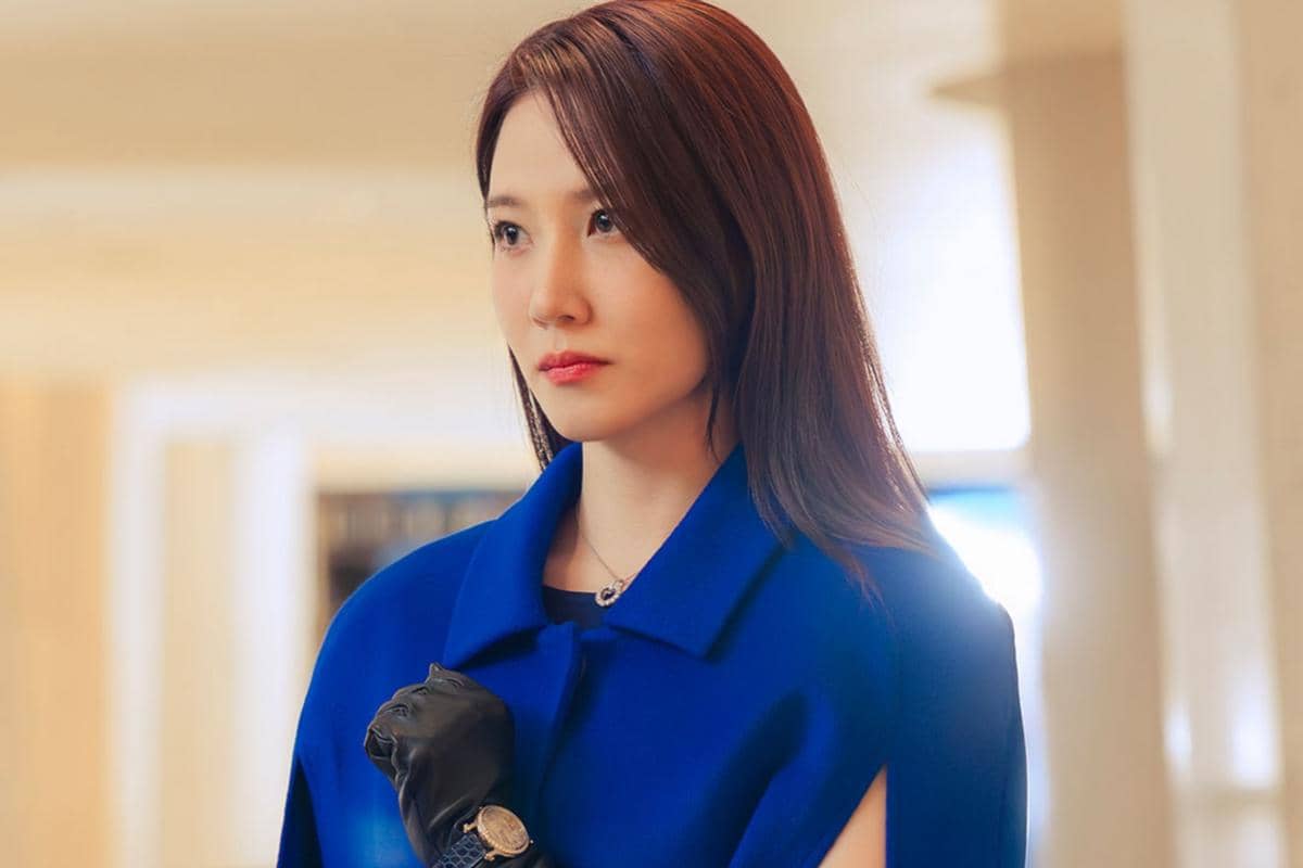 Seorang wanita berambut panjang mengenakan mantel biru dan sarung tangan hitam tampak serius dalam adegan drama Spooky in Love.