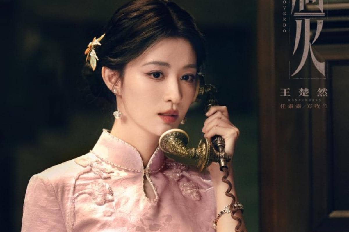 Seorang wanita mengenakan qipao berwarna merah muda sedang berbicara di telepon antik dalam adegan drama Overdo.