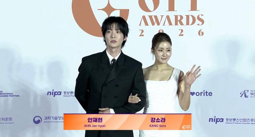 Seorang pria mengenakan setelan jas hitam dan seorang wanita mengenakan gaun putih berpose di karpet merah acara Global OTT Awards 2026.