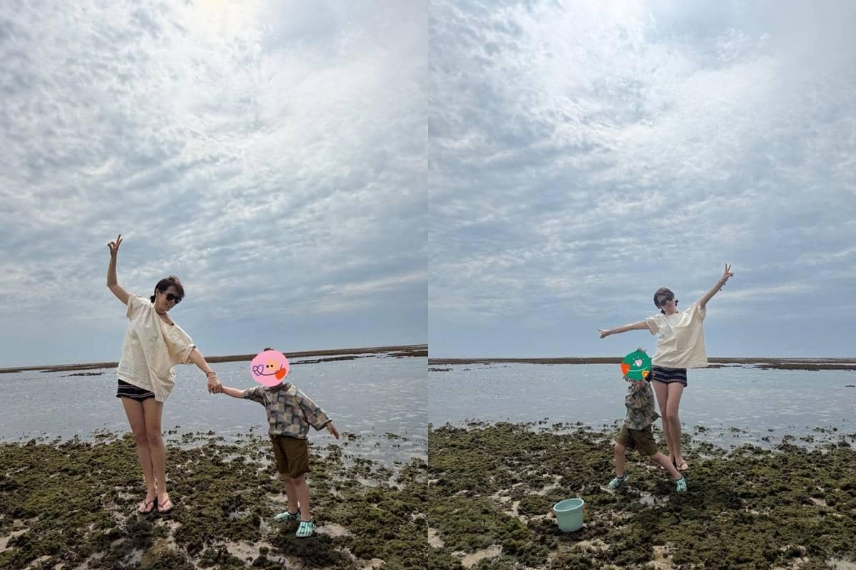 Seorang perempuan berpose ceria bersama anak kecil di tepi pantai berbatu dengan langit berawan dan suasana liburan yang santai.