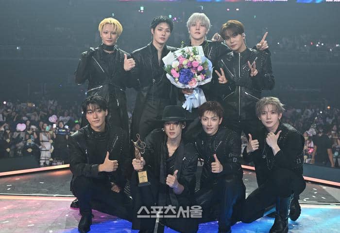 Delapan anggota grup musik ATEEZ berpose di panggung setelah memenangkan penghargaan di Seoul Music Awards 2026 sambil memegang trofi dan buket bunga.