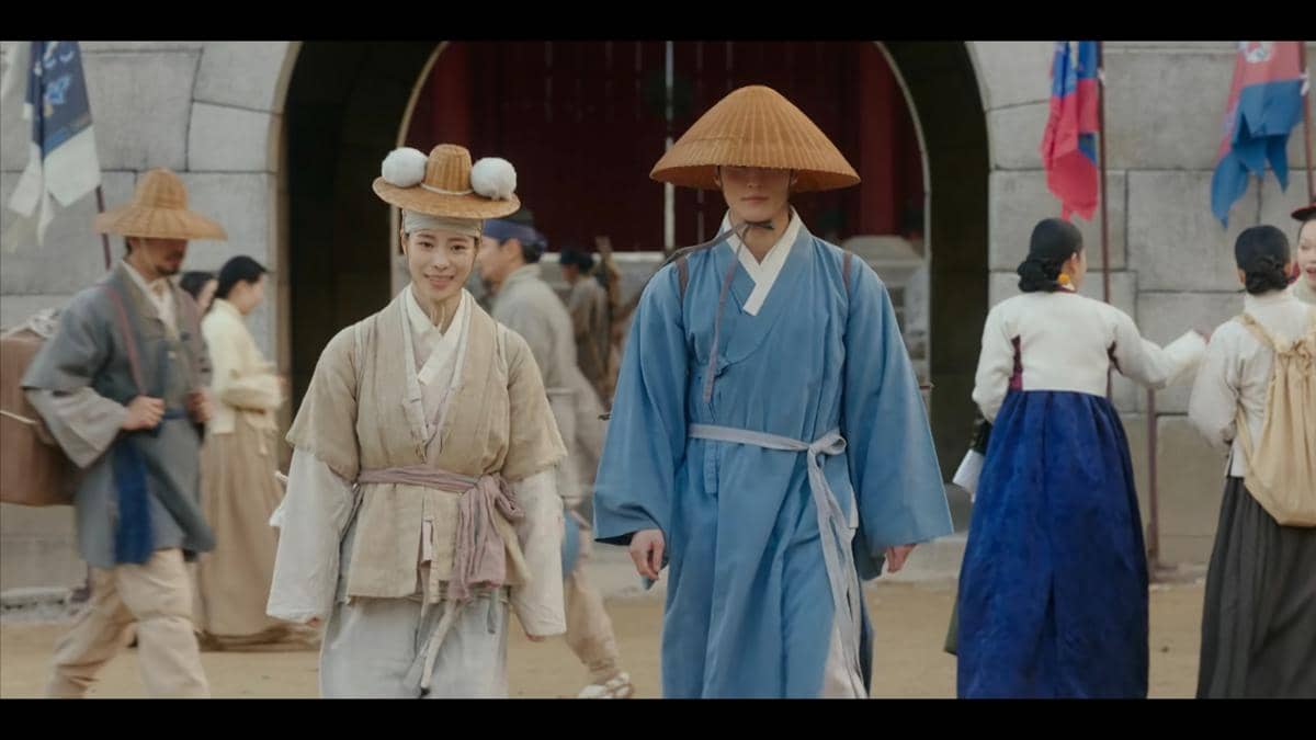 Dua karakter mengenakan hanbok tradisional berjalan di jalanan pasar era kerajaan dalam cuplikan drama My Royal Nemesis.