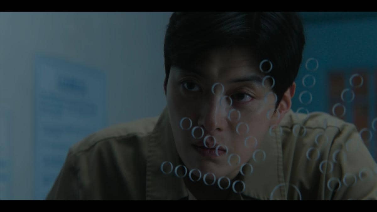 Seorang pria menatap serius melalui kaca dengan pantulan lingkaran cahaya dalam cuplikan drama My Royal Nemesis di Netflix.
