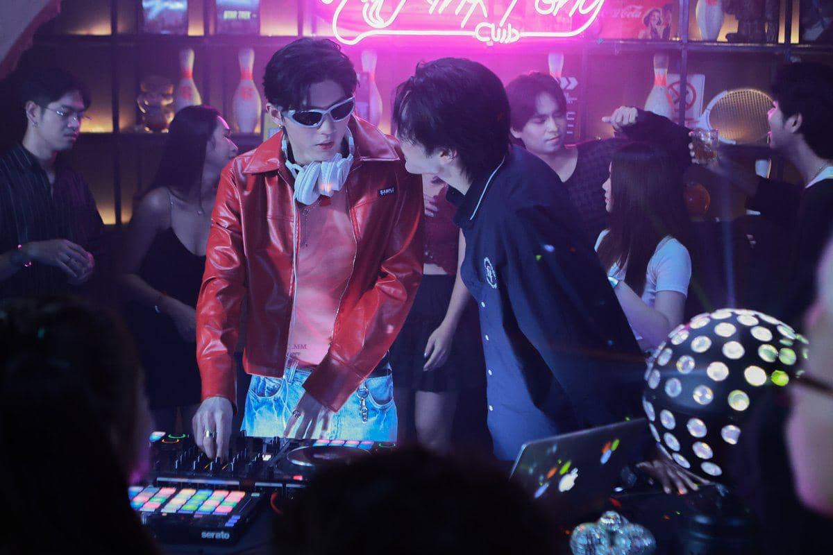Dua pria berbicara di meja DJ dengan lampu neon dan suasana klub malam yang ramai di cuplikan Only Friends: Dream On.