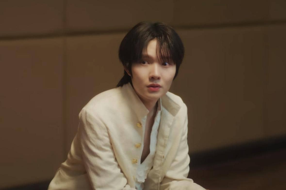 Seorang aktor mengenakan jas putih dengan kancing emas dalam cuplikan drama Still Holding up like the Moon.