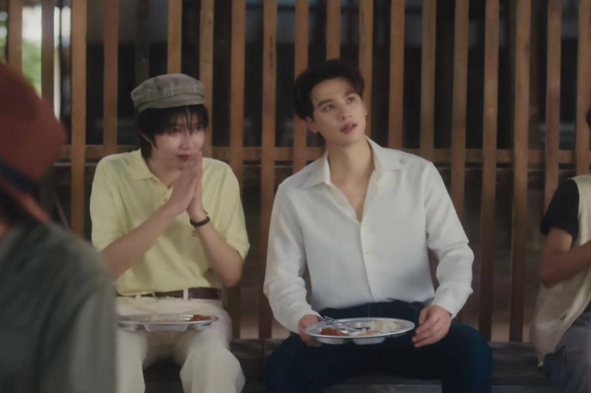 Dua karakter duduk berdampingan sambil memegang nampan makanan dalam cuplikan drama Still Holding up like the Moon.