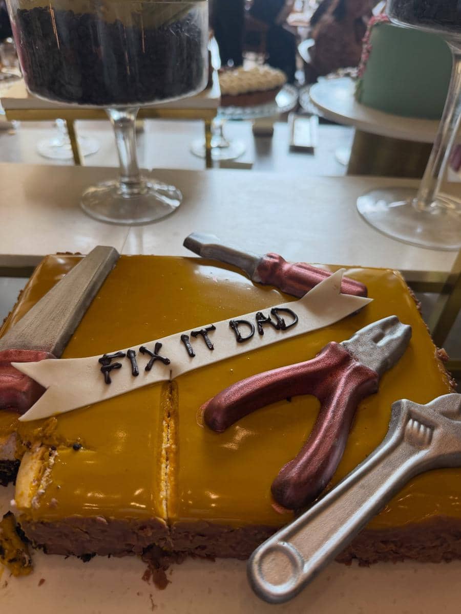 Kue persegi berlapis glasir kuning dengan hiasan fondant berbentuk alat pertukangan dan tulisan 'Fix It Dad' di atasnya.