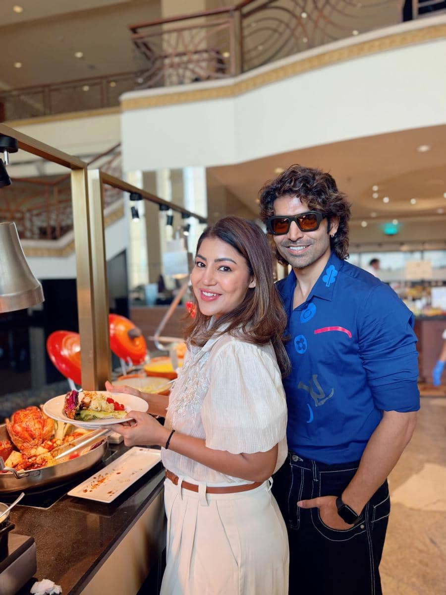 Sepasang pria dan wanita tersenyum sambil mengambil makanan di buffet restoran mewah dengan suasana interior elegan.