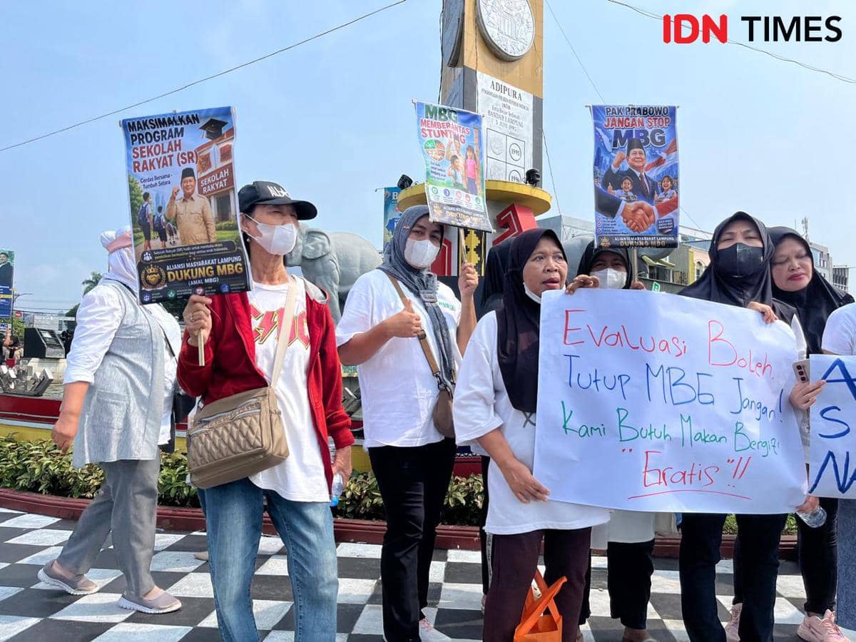 Sejumlah warga membawa poster dan spanduk dukungan terhadap program MBG saat aksi di sekitar Tugu Adipura, mengenakan pakaian kasual dan masker.
