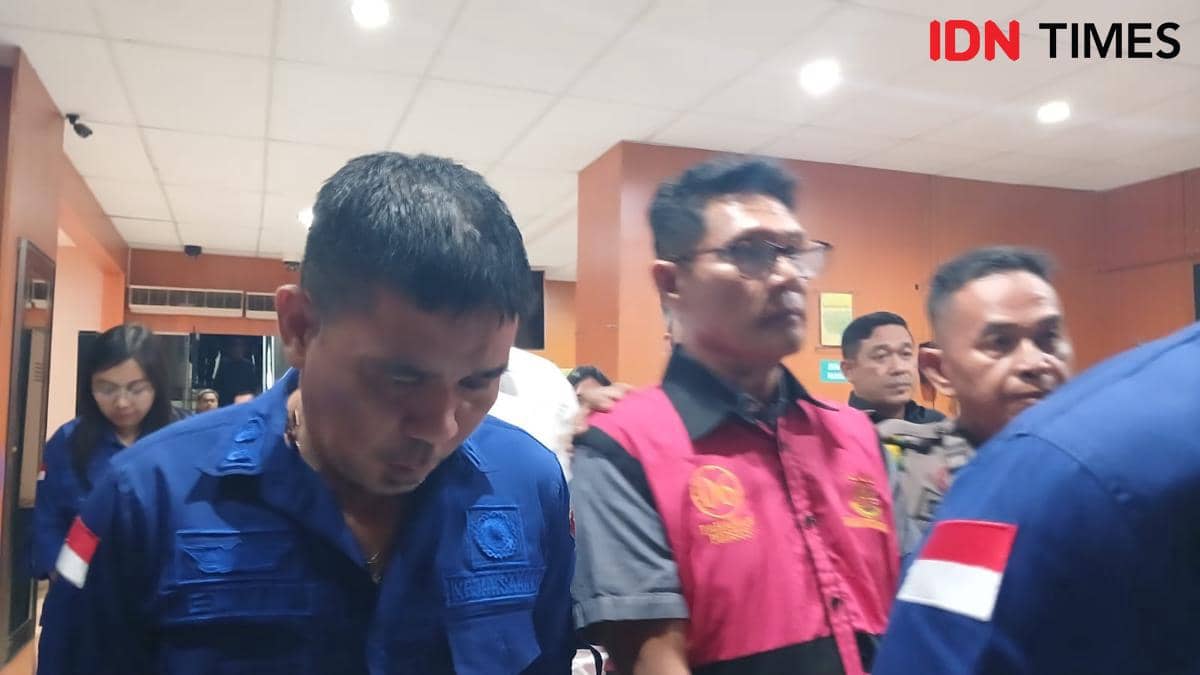 Beberapa pria mengenakan seragam biru dan rompi merah berada di dalam ruangan dengan pencahayaan terang dan dinding berwarna oranye.