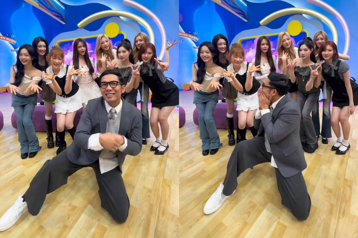 Seorang pria berjas abu-abu berpose ceria bersama sekelompok perempuan di studio dengan latar warna biru dan ungu yang cerah.