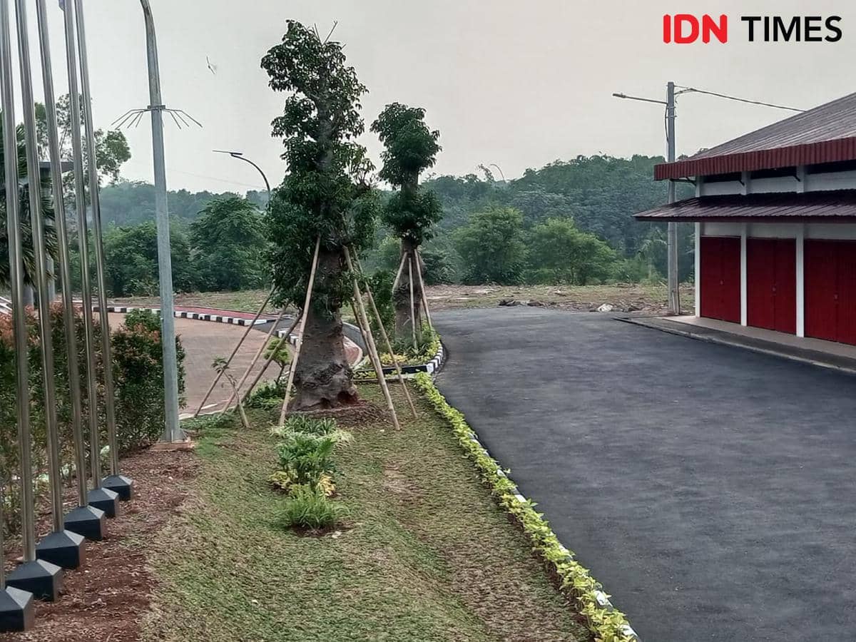 Halaman gedung Kopdes Merah Putih di Pakansari Bogor dengan jalan beraspal, taman hijau, dan deretan pintu berwarna merah.