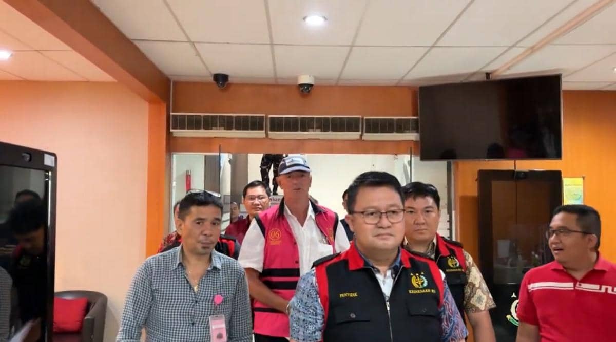 Beberapa petugas Kejati Sulut menggiring seorang pria berbaju putih dan rompi merah muda menuju mobil tahanan di dalam gedung.
