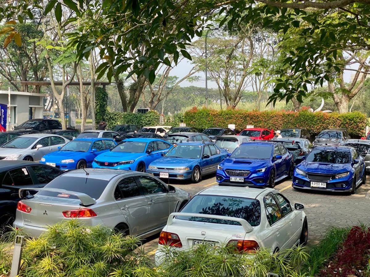 Deretan mobil berbagai warna, didominasi biru dan perak, terparkir rapi di area terbuka dengan pepohonan rindang di sekitar ICE BSD.