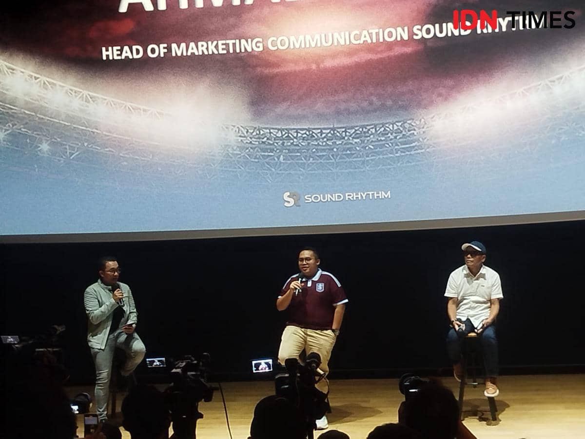 Tiga pria berbicara di atas panggung dalam acara konferensi pers dengan latar layar bertuliskan Sound Rhythm dan stadion di belakangnya.