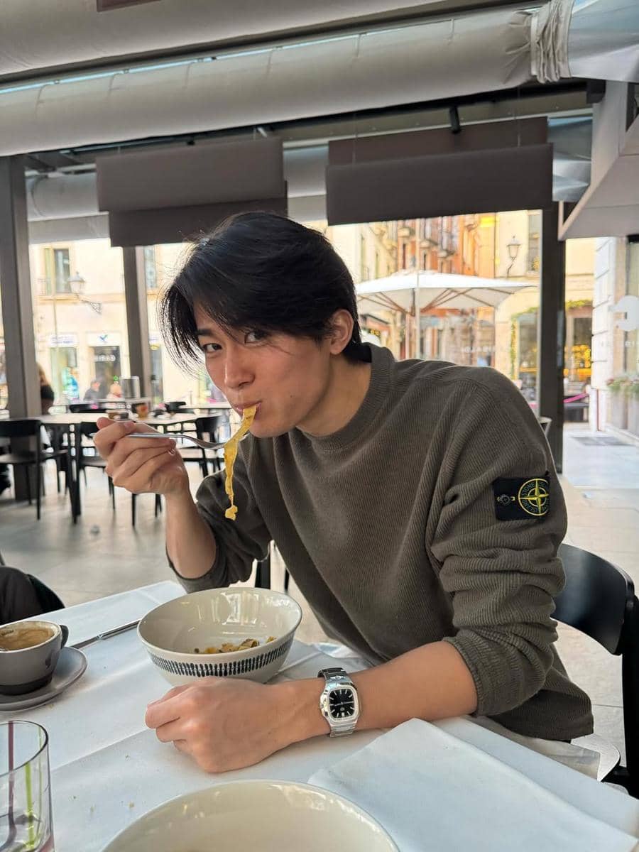 Keito Nakamura berambut hitam mengenakan sweater abu-abu makan pasta di restoran dengan suasana santai dan pencahayaan alami.