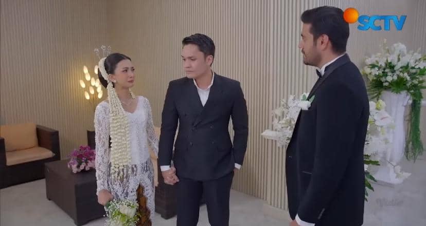 Adegan sinetron menampilkan pasangan pengantin mengenakan busana adat Jawa berbicara dengan pria berjas hitam di ruangan dekorasi bunga.