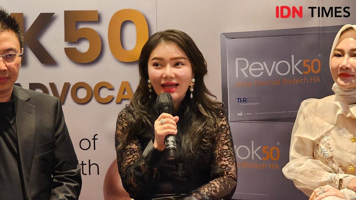 Seorang wanita berbicara memegang mikrofon di acara peluncuran produk perawatan kulit bersama dua orang lainnya di latar bertuliskan Revok50.