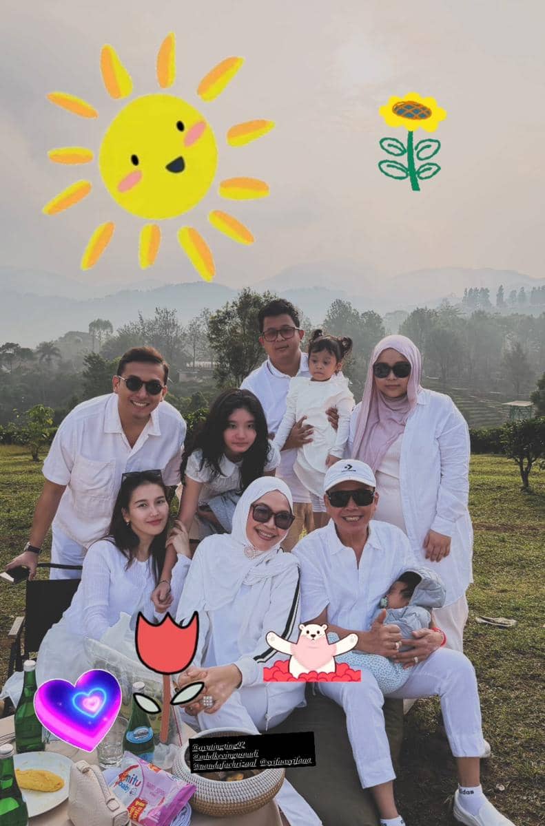 Keluarga berpakaian putih berpose bersama di area hijau Cisarua dengan latar pegunungan dan hiasan gambar matahari serta bunga.