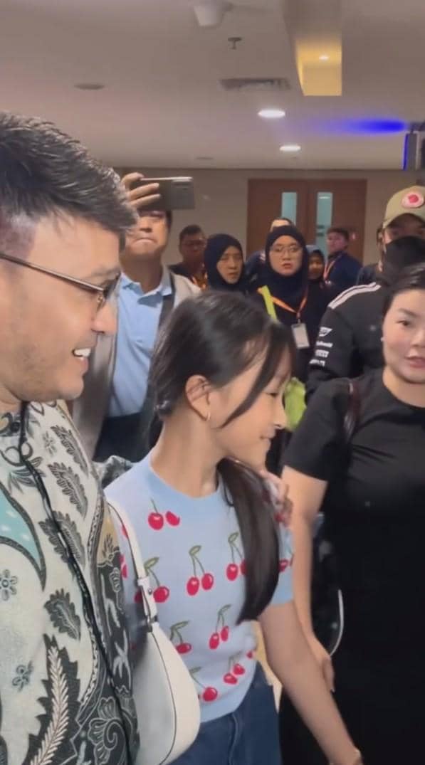 Ruben Onsu tersenyum sambil berjalan bersama seorang anak perempuan berkaus biru bermotif ceri di tengah kerumunan orang di dalam ruangan.