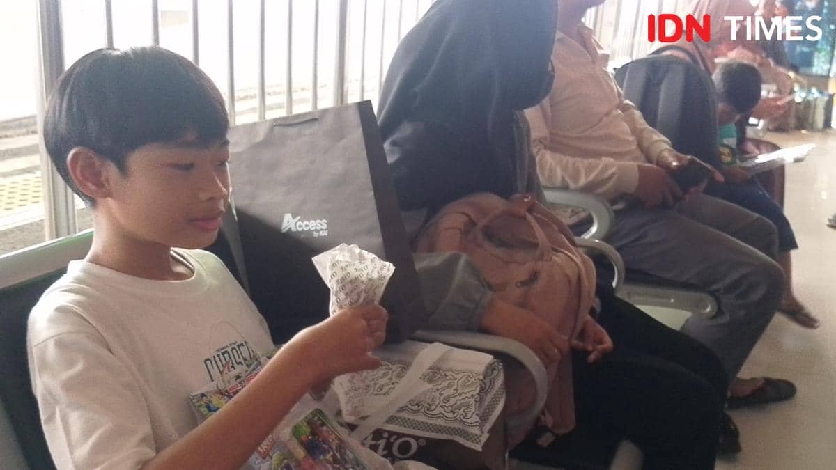 Seorang anak duduk di ruang tunggu Stasiun Purwokerto bersama penumpang lain saat musim libur sekolah, memegang makanan ringan di tangannya.
