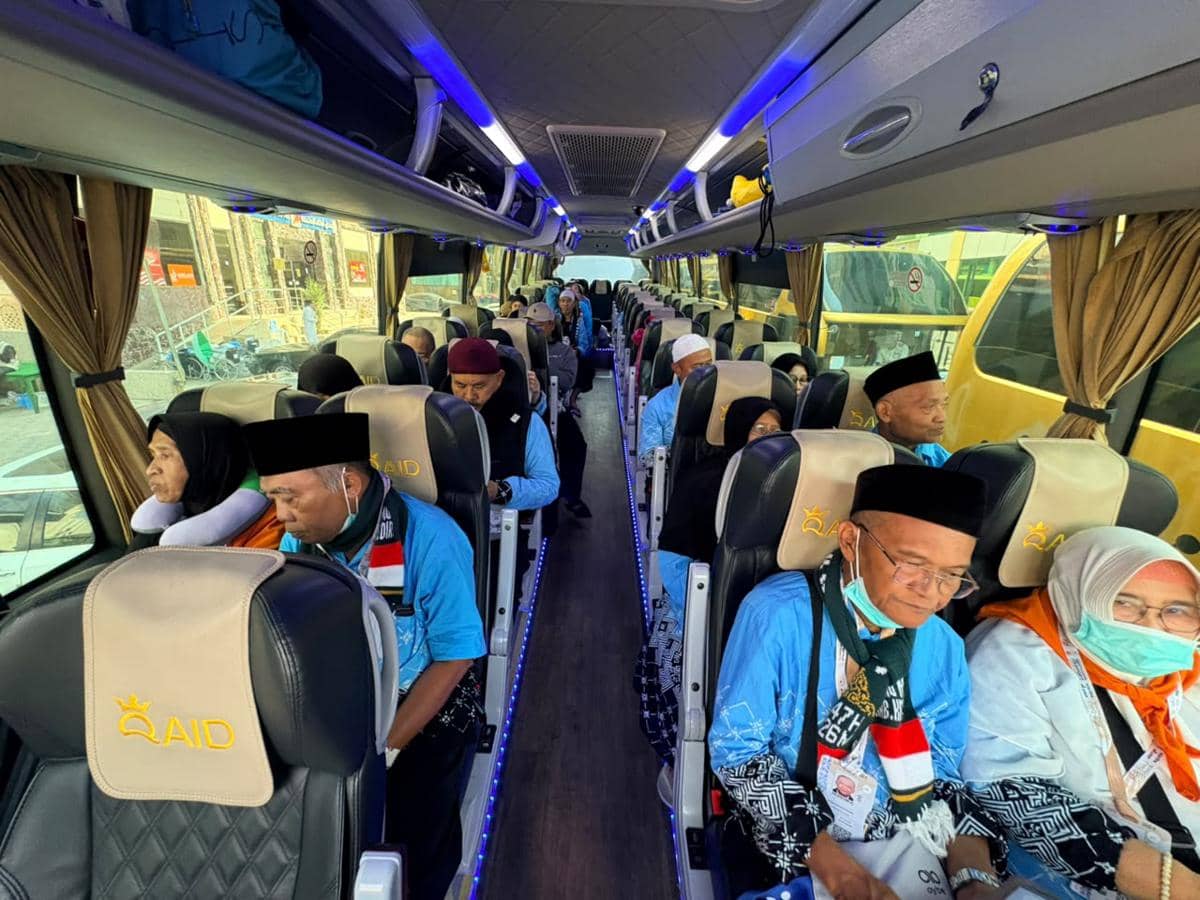 Jemaah haji Kloter UPG 43 duduk di dalam bus menuju Madinah dari pemondokan di Misfalah, Makkah, mengenakan seragam biru dan perlengkapan haji.