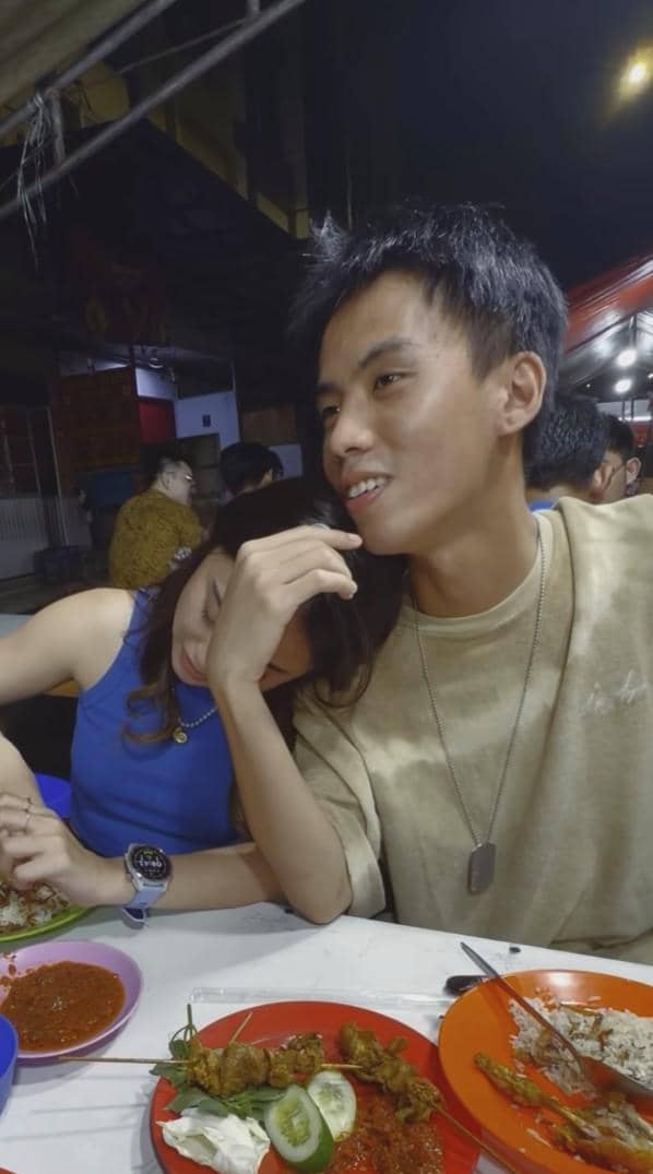 Yuka dan Michelle duduk di warung makan malam hari, perempuan bersandar di bahu pria sambil menikmati sate dan sambal.