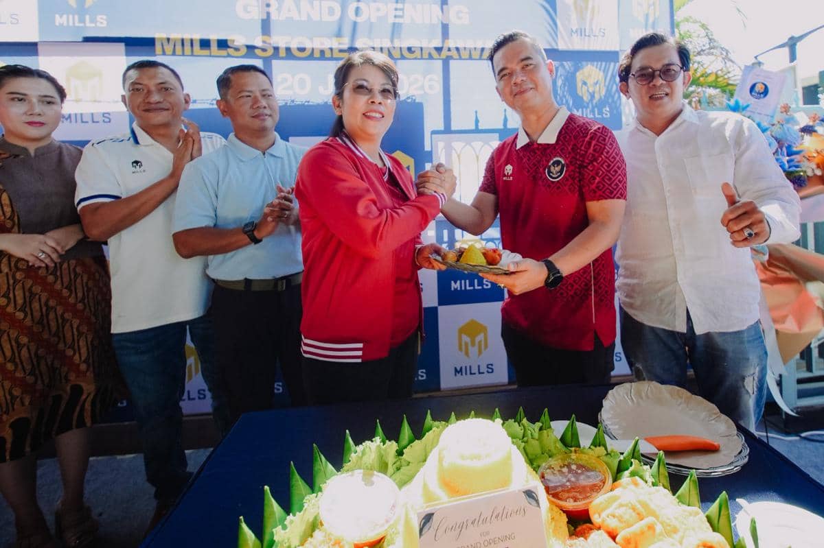 Beberapa orang berpose sambil berjabat tangan di acara pembukaan toko Mills di Singkawang dengan tumpeng di meja depan.