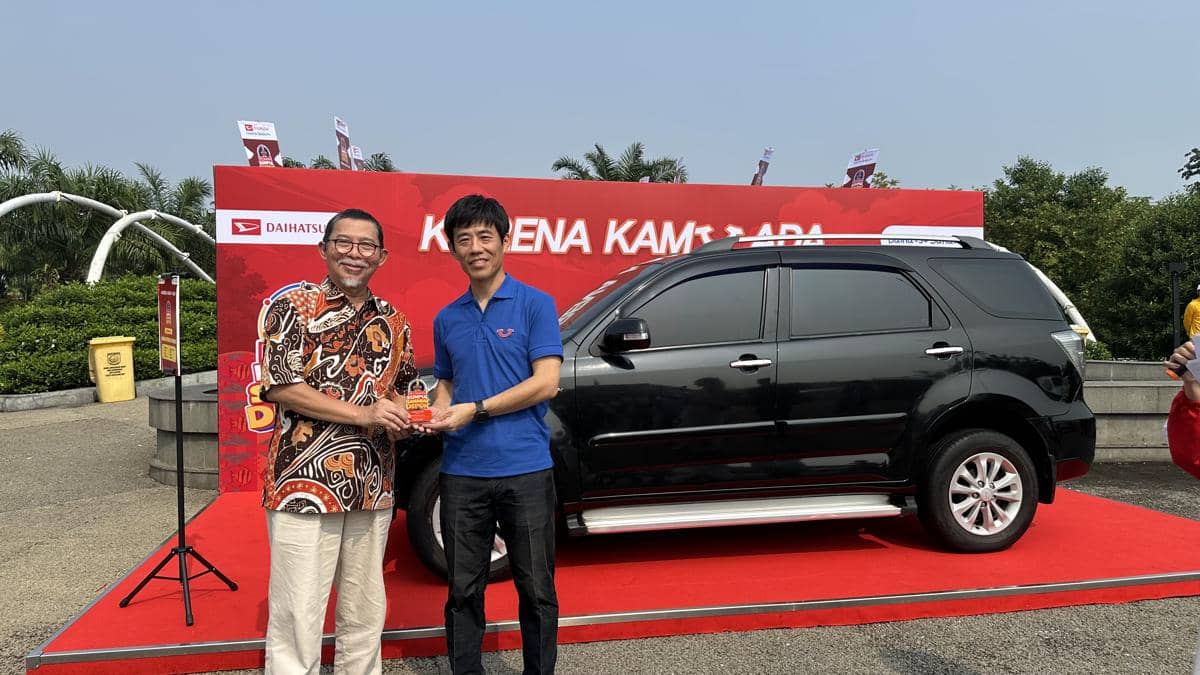 Dua pria berpose di depan mobil Daihatsu Terios hitam saat penyerahan penghargaan di atas karpet merah dengan latar spanduk merah.