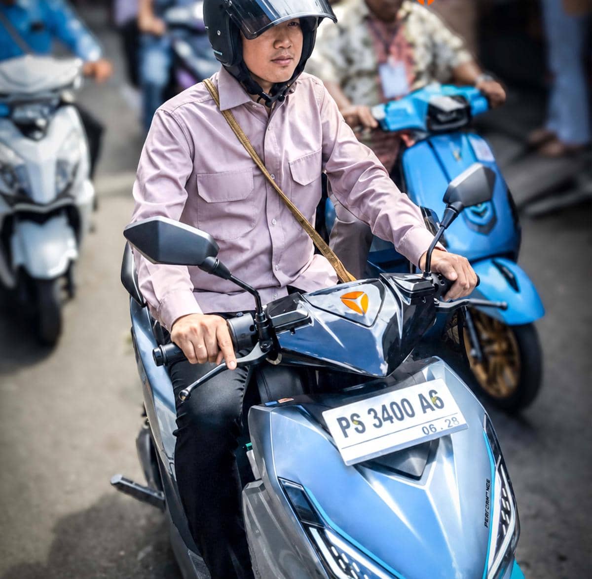 Seorang pria mengenakan helm hitam dan kemeja ungu muda sedang mengendarai motor listrik Yadea Velax di jalan.