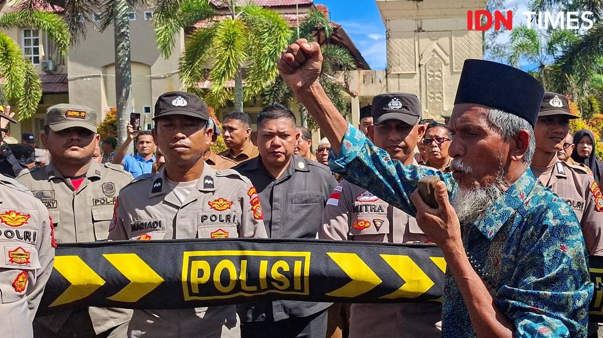 Seorang pria mengangkat tangan saat unjuk rasa di depan barisan polisi yang berjaga di Kantor Bupati Nagan Raya, Kecamatan Beutong Ateuh Banggalang.