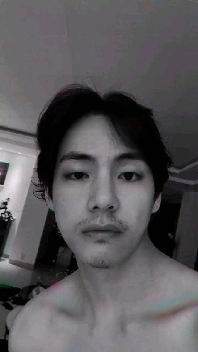 Seorang pria berambut hitam dengan kumis tipis berpose tanpa baju di dalam ruangan dengan pencahayaan redup.