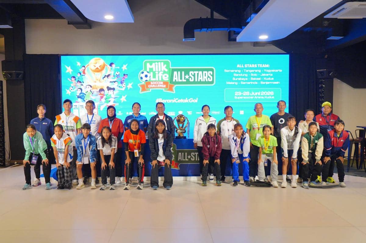 Para peserta dan pelatih berfoto bersama di depan layar bertema Milk Life Soccer Challenge All Stars 2026 dengan trofi di tengah ruangan.