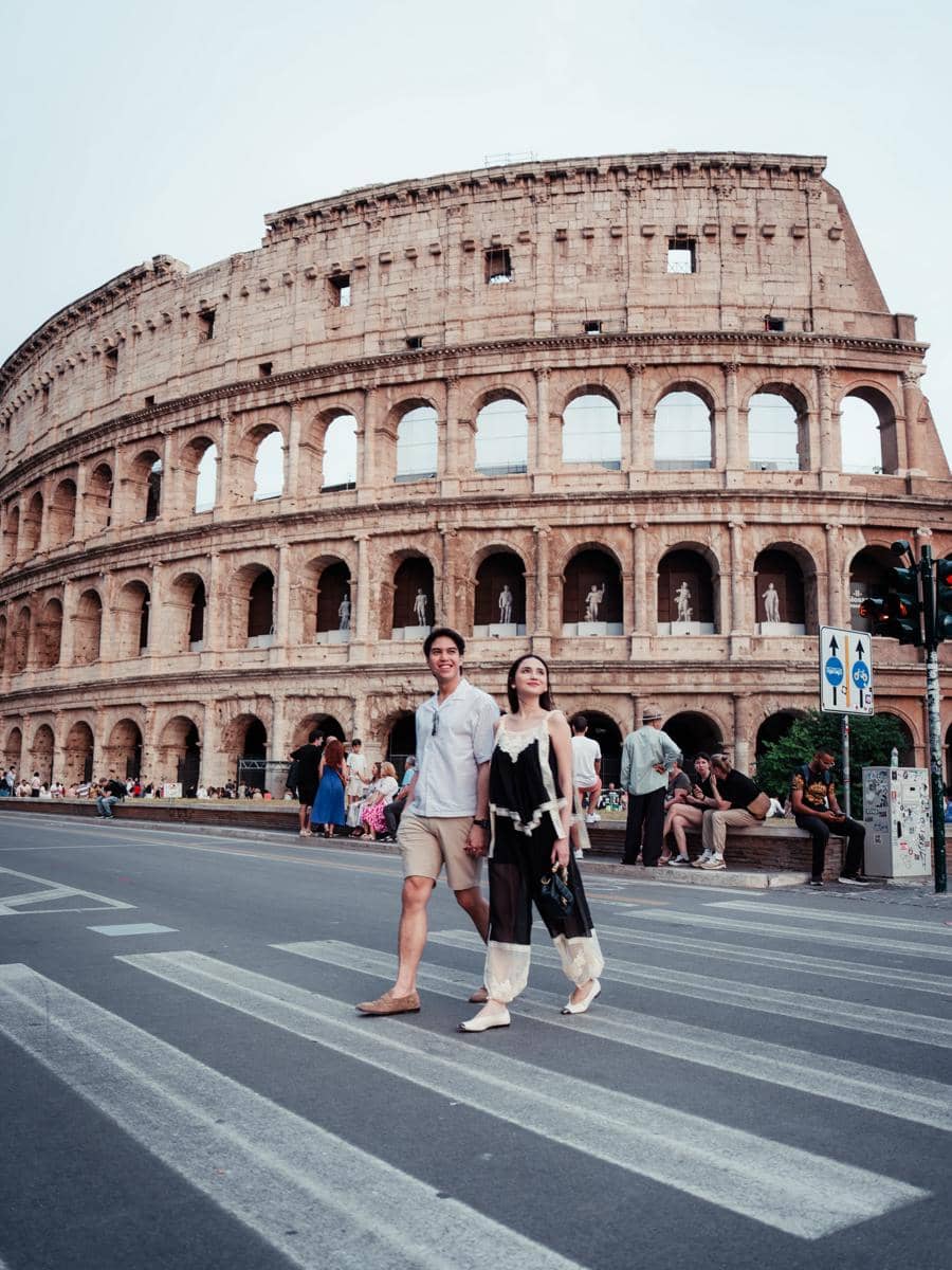 Sepasang wisatawan berjalan berpegangan tangan di depan Colosseum Roma, Italia, saat liburan musim panas di Eropa.