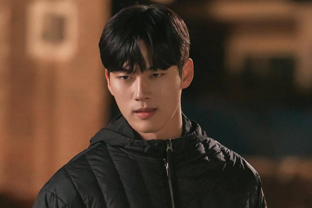 Seorang pria berjaket hitam berdiri di malam hari dengan ekspresi serius dalam adegan drama Doctor on the Edge.