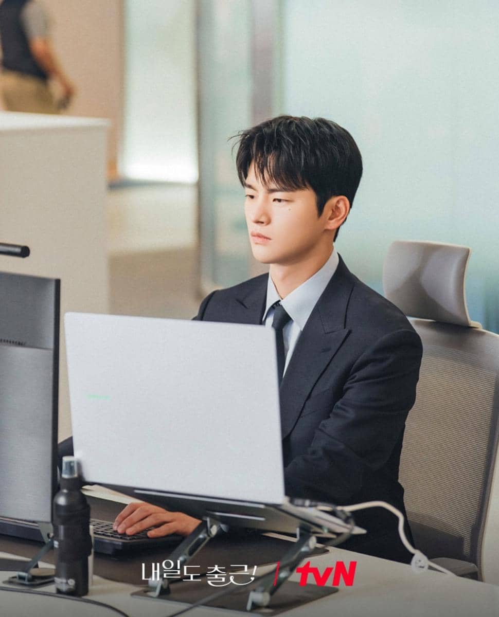 Seorang pria mengenakan setelan jas hitam sedang bekerja di depan laptop di meja kantor modern dengan suasana profesional.