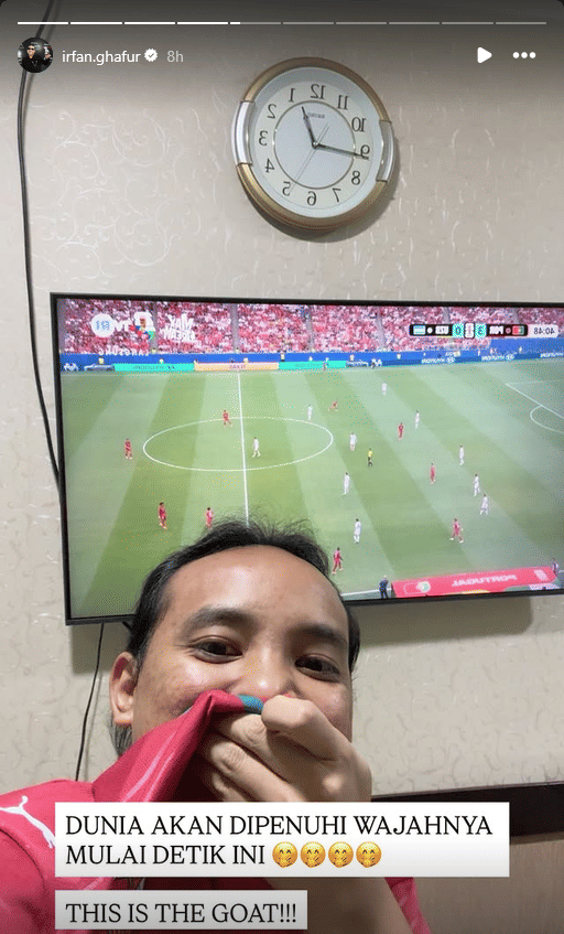 Seorang pria berpose di depan televisi yang menayangkan pertandingan sepak bola Piala Dunia 2026 sambil menutupi mulut dengan kausnya.