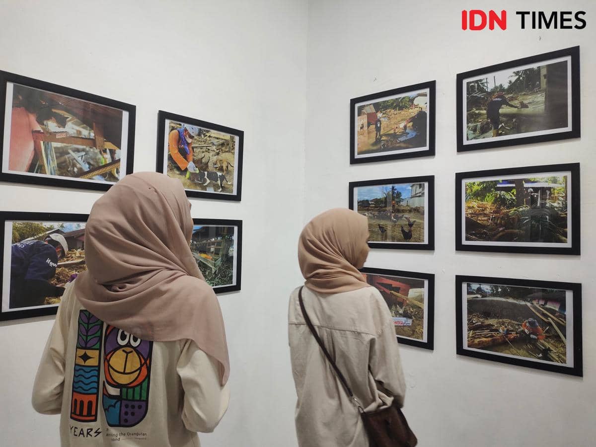 Dua pengunjung melihat deretan foto bertema penyelamatan satwa korban banjir Sumatra dalam pameran yang digelar Centre for Orangutan Protection.