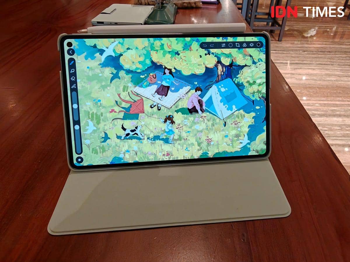 Tablet HUAWEI MatePad Mini diletakkan di atas meja kayu dengan layar menampilkan ilustrasi berwarna cerah bertema alam.